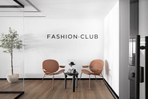 חלל הכניסה במשרדי Fashion Club באור יהודה: קיר עם לוגו המותג, שתי כורסאות בגוון טרקוטה ושולחן צד עגול