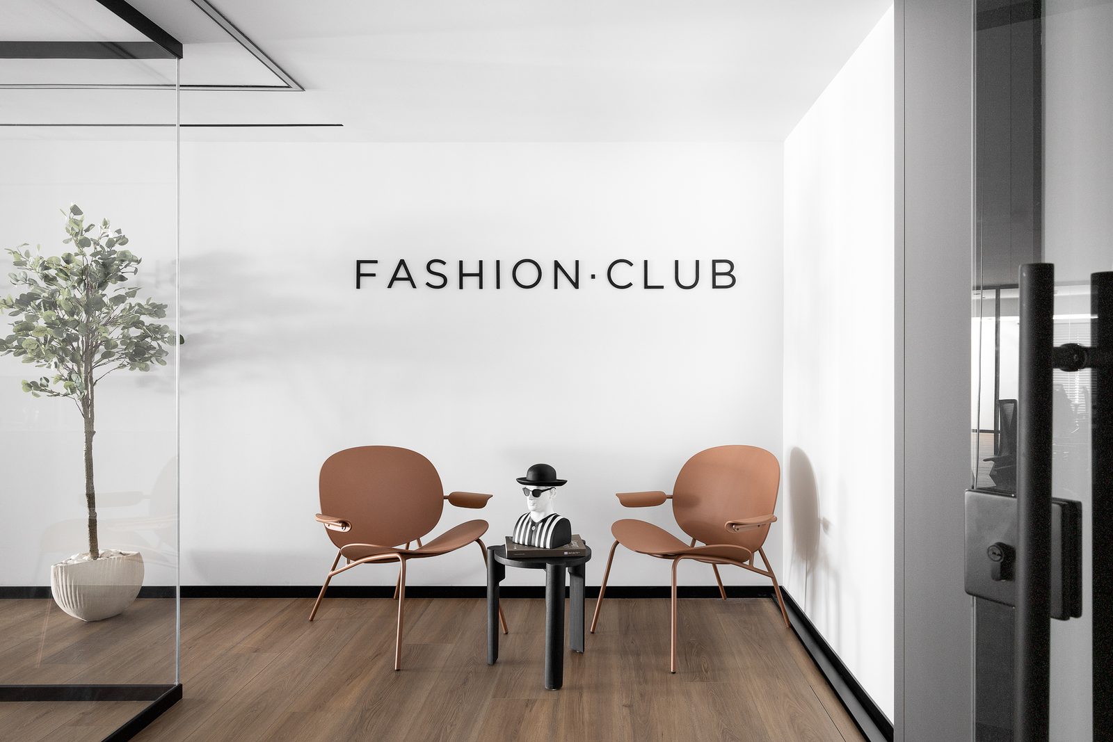חלל הכניסה במשרדי Fashion Club באור יהודה: קיר עם לוגו המותג, שתי כורסאות בגוון טרקוטה ושולחן צד עגול